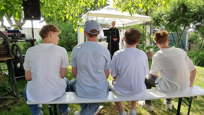 Vier Jugendliche auf einer Bank im Garten unter Bäumen hören Musik.