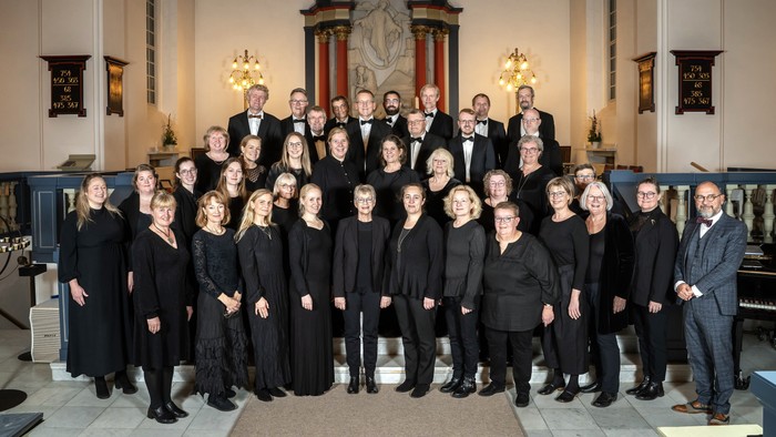 En stor gruppe af korister poserer sammen i en kirke.