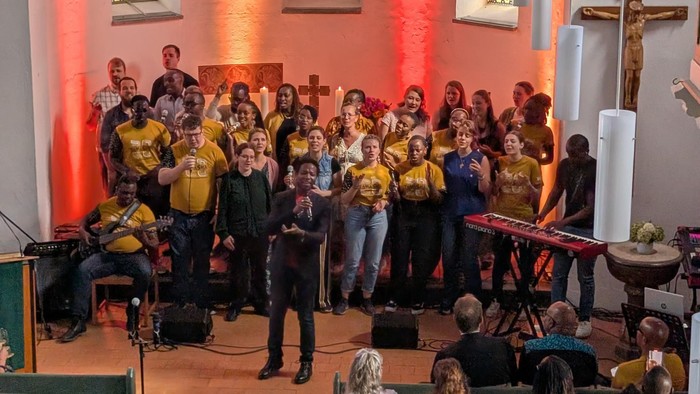 Eine Gruppe singt in einer Kirche, begleitet von Musikern und einem Publikum.