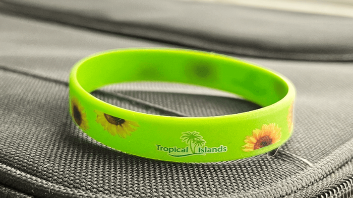Ein Armband aus Silicon mit Sonneblumenmuster liegt auf einer Laptophülle. Das Armband liegt vorne an einer Ecke und füllt das halbe Bild aus. Es ist hellgrün.