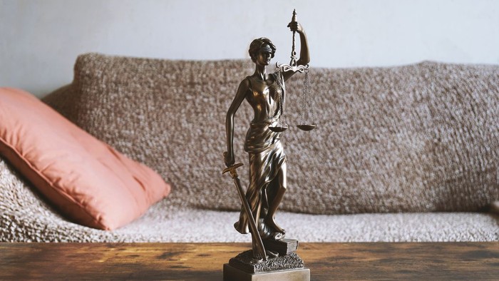 Die Statue einer Frau mit Waage auf einem Holztisch vor einem Sofa.