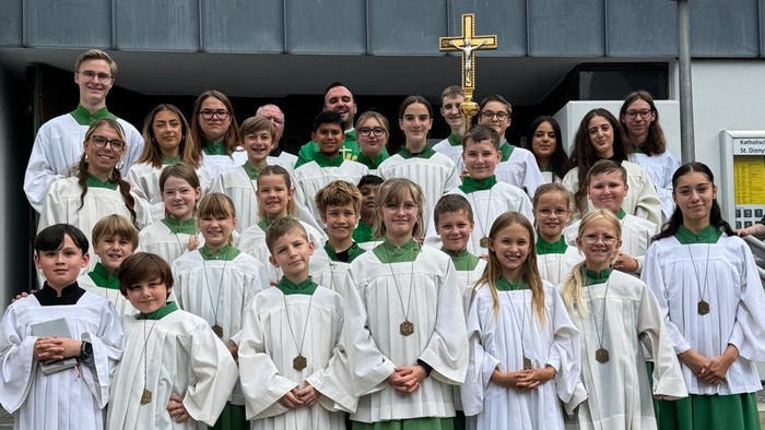 Eine Gruppe von Kindern und Erwachsenen in weißen und grünen Roben posiert vor einem Gebäude mit Kreuz.