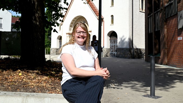 Frau sitzt vor weißem Gebäude mit Kirche im Hintergrund