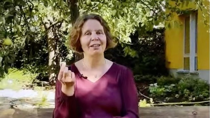 Foto von Pfarrerin Claudia Mieth auf einer Bank sitzende in die Kamera sprechend. In der Hand hält sie einen Stein - ein Souvenir aus dem Urlaub.