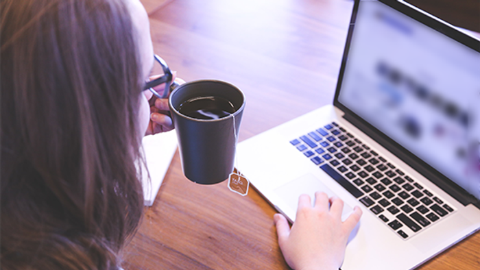 Frau arbeitet an Laptop mit Kaffeetasse auf dem Tisch