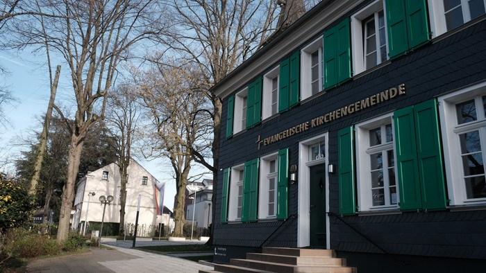Das Bild zeigt ein Gebäude mit grünen Fensterläden und einem Schild