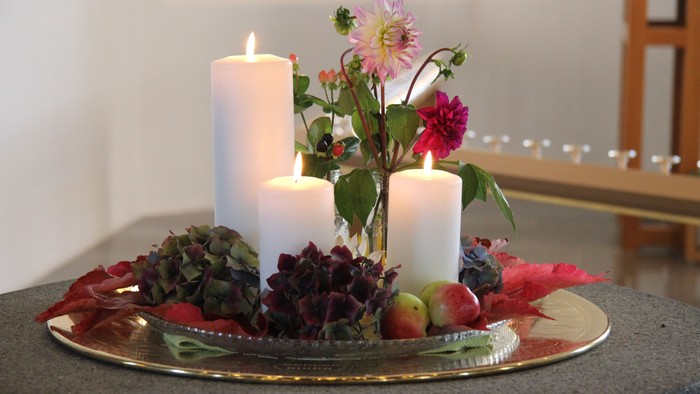 En festlig hyggelig stilleben med lysende lygter, blomster og frugter på en gul plate.