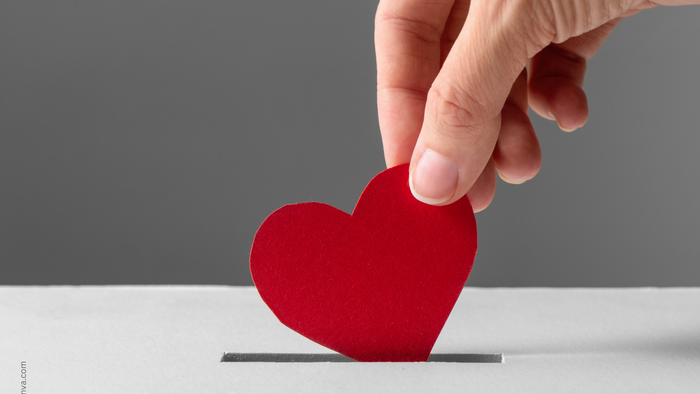 Eine Hand platziert ein rotes Herz auf einem kleinen Ständer.