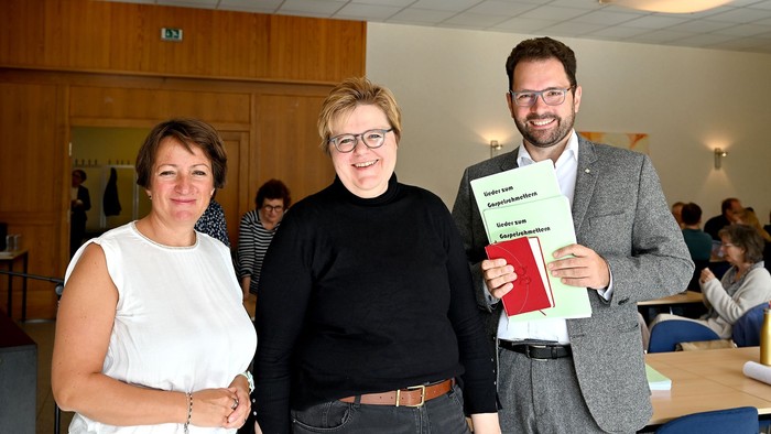 Drei Personen posieren mit einem Buch, eine davon hält es hoch