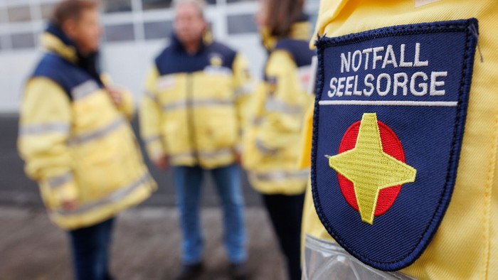 Drei Personen in gelben Jacken mit Notfall Seelsorge Abzeichen.