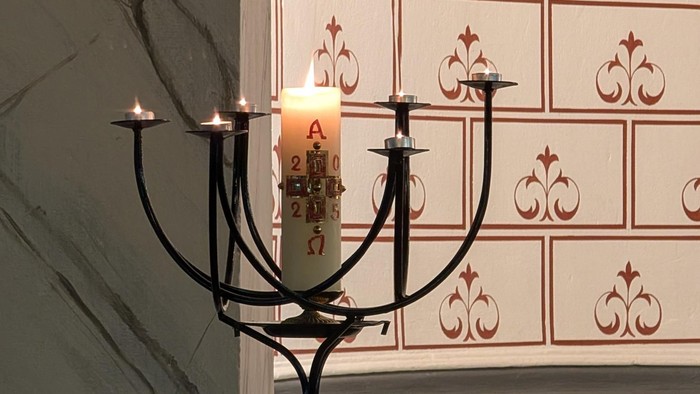 Kerzenleuchter mit brennender Kerze vor verzierter Wand