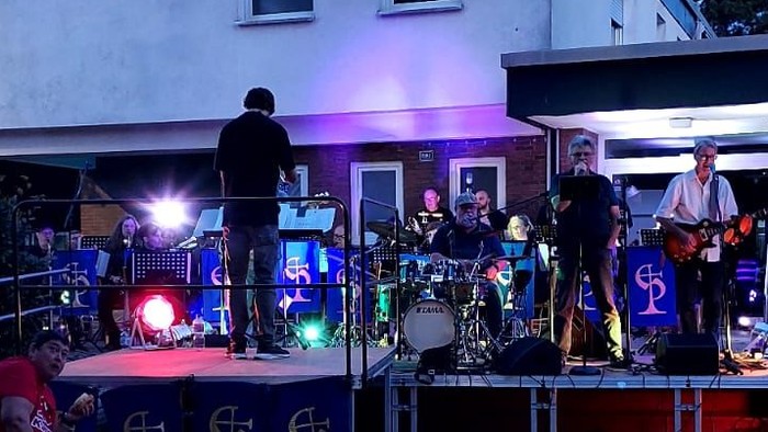 Eine Band spielt abends auf einer Bühne vor einem Haus.
