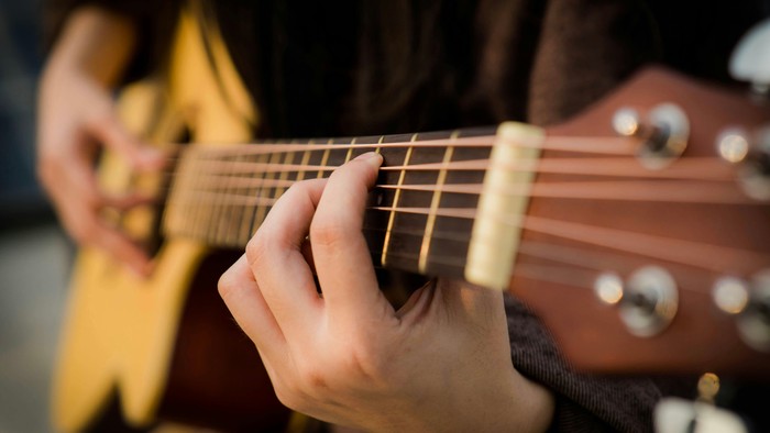 Eine Person spielt eine Gitarre und greift einen Akkord.