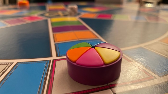 Ein bunter Würfel liegt auf einem Spielbrett.