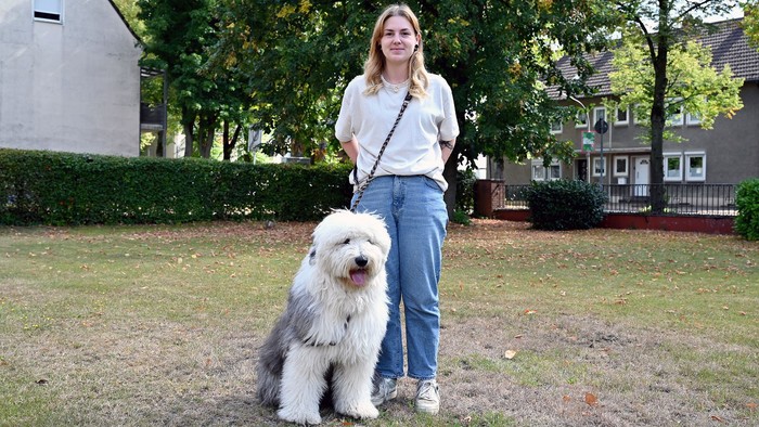 Junges Mädchen mit weißem Hund auf Wiese vor Häusern