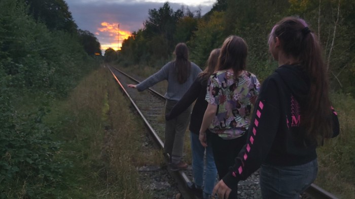 Drei Jugendliche gehen bei Sonnenuntergang auf Eisenbahnschienen