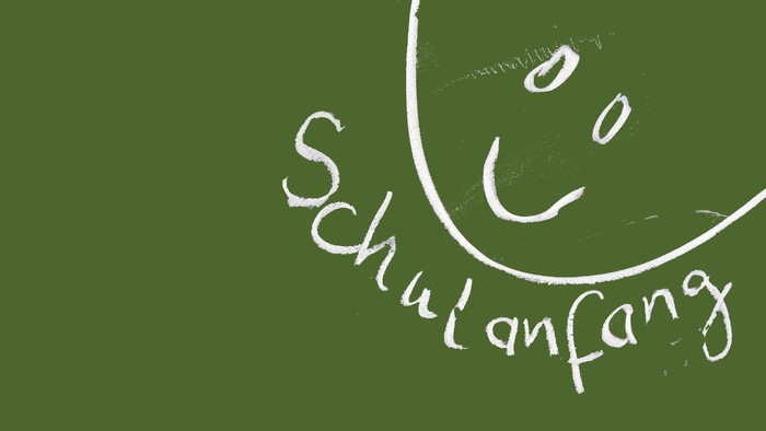 Kreidezeichnung eines Lachgesichtes mit Text 'Schulanfang' auf grüner Fläche
