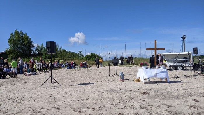 Blauer Himmel, heller Sand, Menschen und ein Altar am Strand.