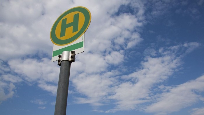 Ein grün-weißes H-Kennzeichen an einem Pfahl vor blauem Himmel mit Wolken.