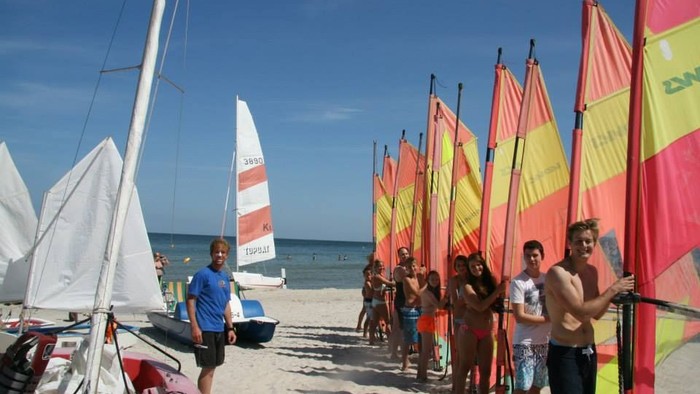 Gruppe von Menschen am Strand, die Segelbretter und Windsurf-Ausrüstung für eine Session am Meer vorbereiten.