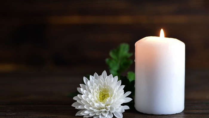 White candle lit next to a single white flower on a wooden surface