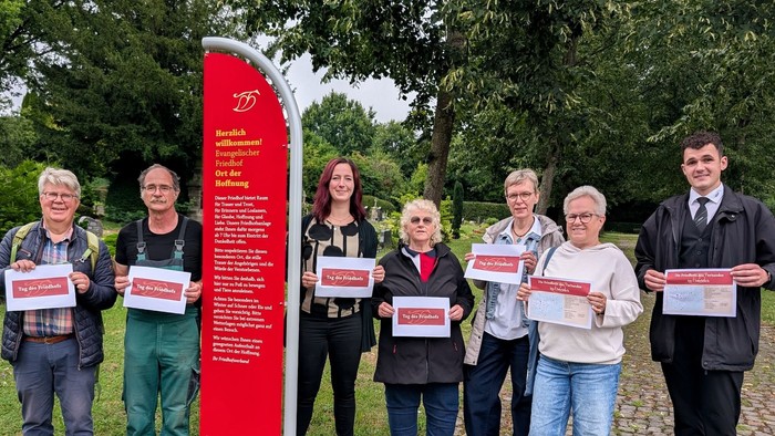 Eine Gruppe Menschen auf einem Friedhof halten Plakate zum Tag des Friedhofs hoch.