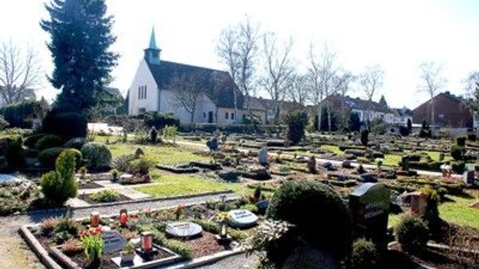 Ein Friedhof mit vielen Gräbern und einem weißen Kirchgebäude im Hintergrund.