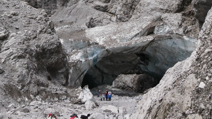 Ein Gruppe von Wanderern erkundet eine felsige Schlucht mit einem Wasserfall im Hintergrund