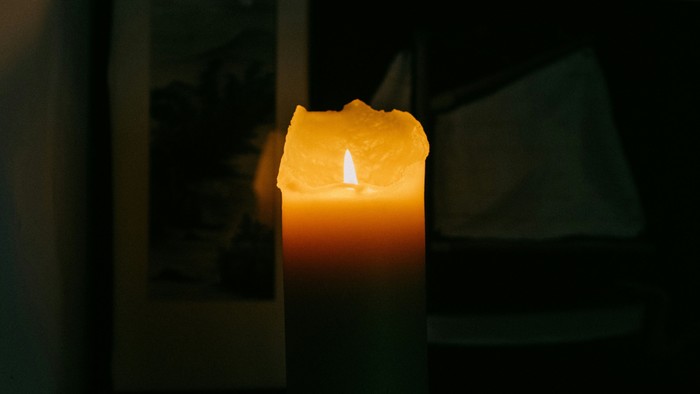 Eine brennende Kerze steht auf einem Regal neben einem gerahmten Bild.