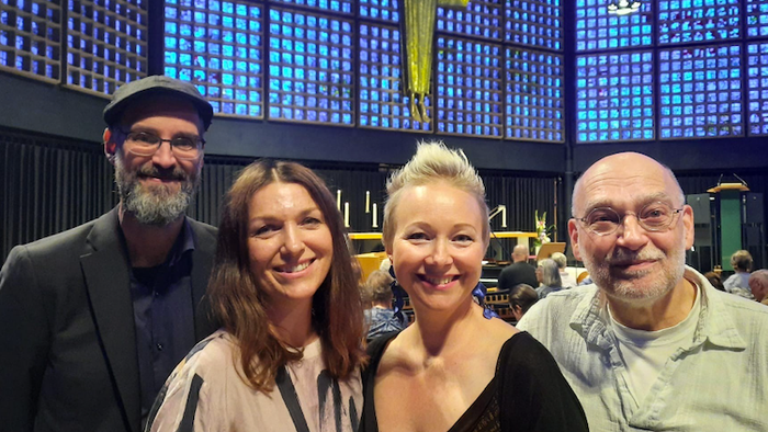 Vier Personen posieren gemeinsam in einer Kirche vor einem bunten Bleiglasfenster.