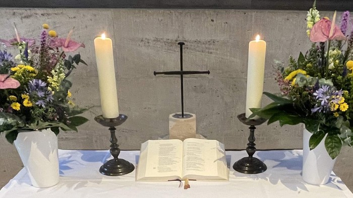Ein Altar mit zwei Kerzen, einem Kreuz und zwei Blumenarrangements