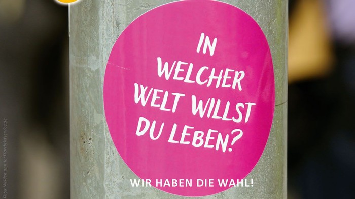 ein metallischer Zylinder mit einem pinken Aufkleber, auf dem steht: „In welcher Welt willst du leben? Wir haben die Wahl!“ Oben rechts das Logo der Pfarrei.