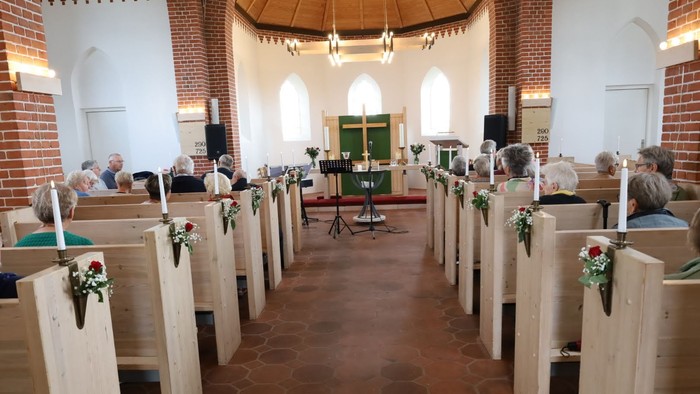 Kirken er dekoreret til en bryllupsceremoni med blomster og grønne elementer.