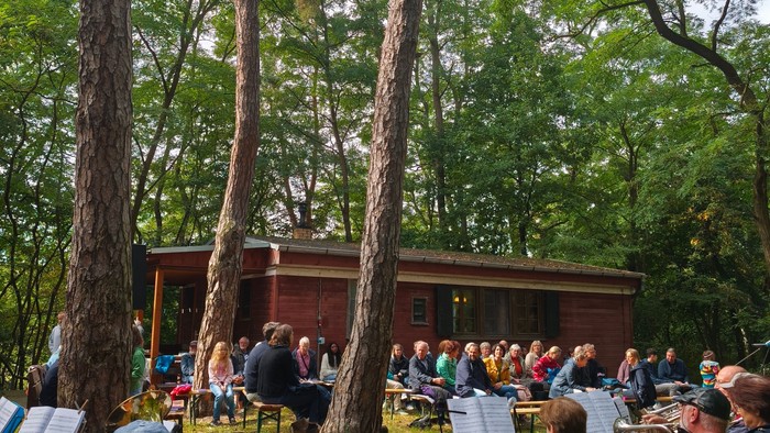 Ein Posaunenchor spielt im Wald, im Hintergrund Zuhörer.