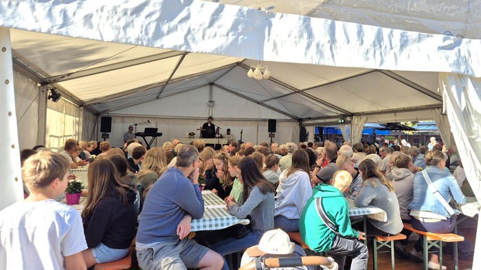 Man sieht viele Gottesdienstbesucher im Zelt an Bierzeltgarnituren sitzen.