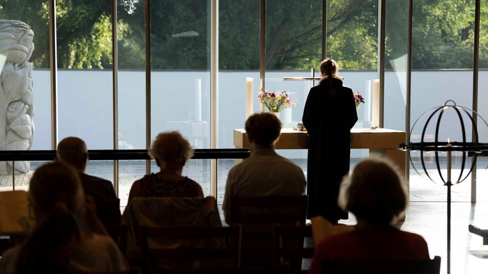 En præst holder et tale i en lys kirke med en gruppe tilhørere.