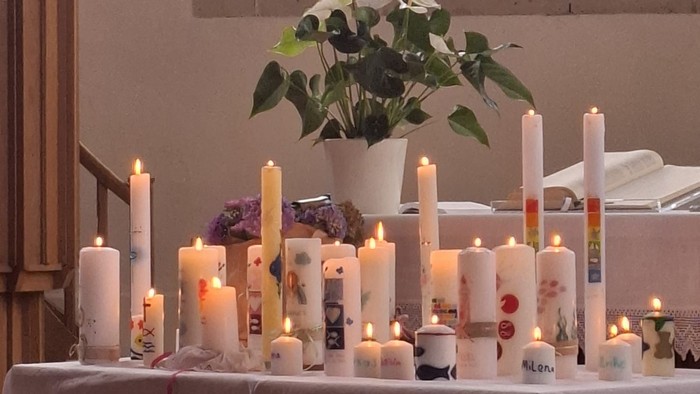 Ein Tisch mit vielen brennenden Kerzen und einer Vase mit Blumen davor