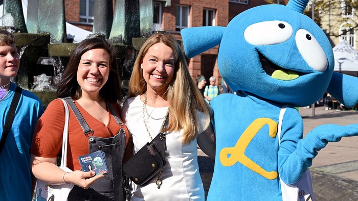 Zwei Frauen posieren mit einem blauen Maskottchen auf der Straße