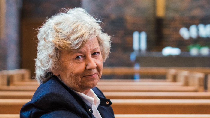 En kvinde sidder i en kirkebænk og smiler.