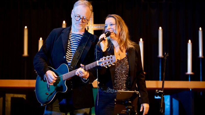 Ein Mann spielt Gitarre, während eine Frau singt, beide auf einer Bühne mit Kerzen.