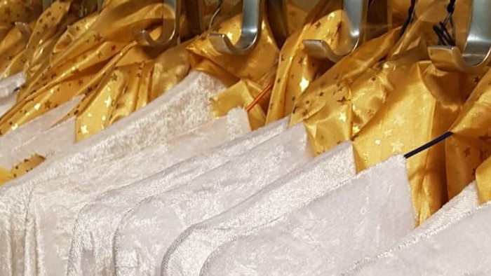 Weiße Kleider mit goldenen Bändern hängen im Laden