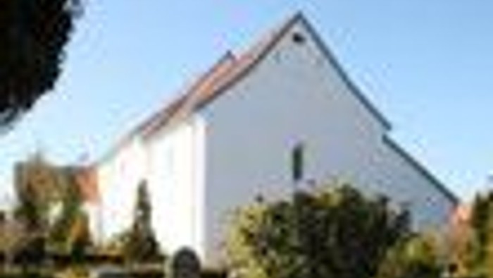 En hvid kirke med to tårne og grønne træer foran