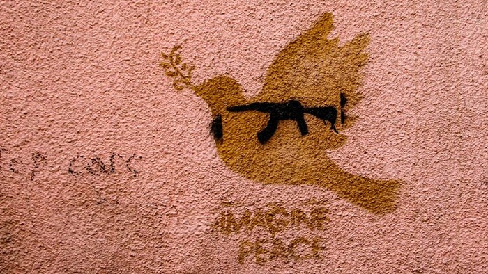 Stencil: Friedenstaube mit Maschinengewehr im Innern. Schriftzug