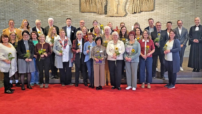 In einer Kirche stehen viele Menschen mit Blumen in den Händen. Am Rand steht eine Pfarrerin.