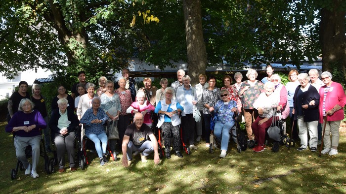 Eine große Gruppe von Senioren haben sich zum Gruppenbild unter einem Baum versammelt.
