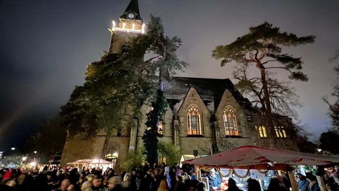 Nächtlicher Weihnachtsmarkt vor historischem Gebäude mit Uhrturm und vielen Menschen