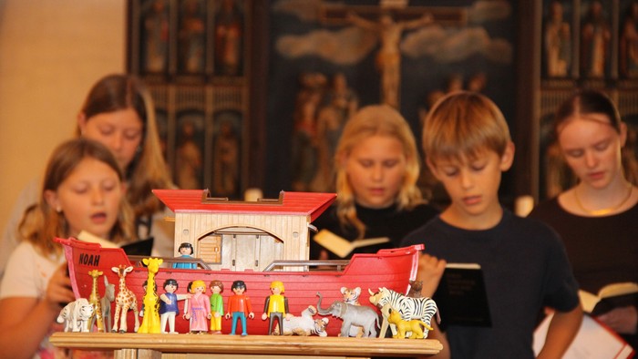 I forgrunden ses en lille Noas ark med mennesker og dyr (playmobil), bagved synder kirkekoret og bagerst ses altertavlen