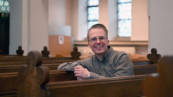 Mann sitzt in Kirchenbank und lächelt.