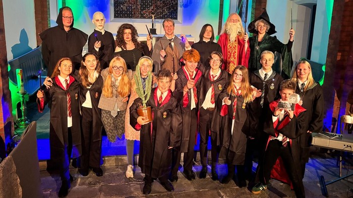 Eine Gruppe von Menschen in Harry-Potter-Kostümen posiert vor einem blauen Hintergrund.