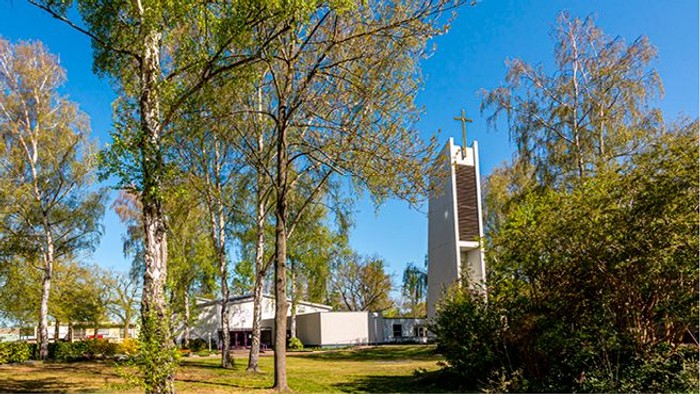 Kirche mit hohem Turm in parkähnlichem Gelände mit Bäumen